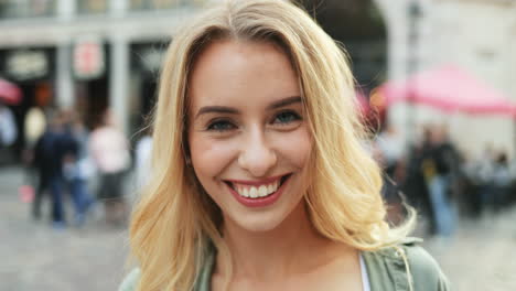 Portrait-of-the-beautiful-blonde-young-woman-looking-straight-to-the-camera,-then-taking-a-photo-on-the-camera.-In-the-center-city.-Close-up.